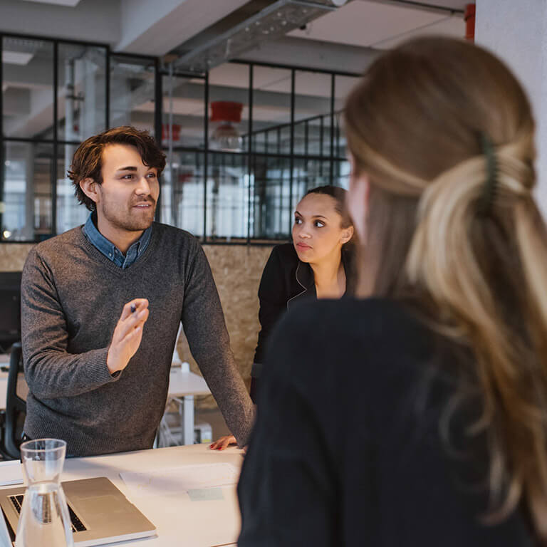 A man speaks to two women in an office setting.